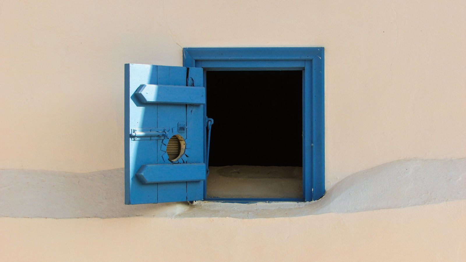 An open blue wooden shutter set into a cream wall