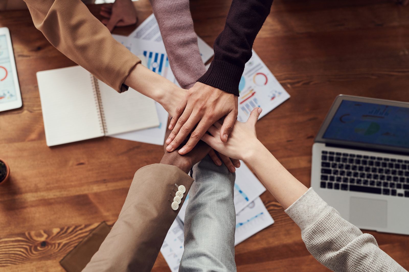 Four colleagues joining hands over a desk of printed charts